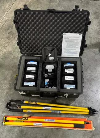 Open pelican case with five Emlid Reach RS2 receivers and survey poles in front.