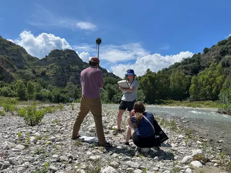 Three students in the field by a river using GNSS to survey in a GCP.