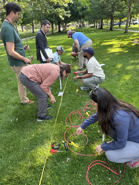Half a dozen workshop participants on a grassy quad in the process of installing geophones in the ground.
