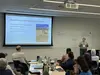 Person at the front of a classroom presenting to other workshop participants about their day's findings. Slide behind her says "We has some learning opportunities".
