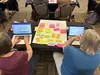 Two project authors working on their laptops which refering to a large post-it sheet of brainstorming ideas.