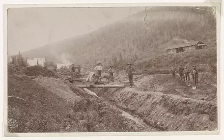 Several gold miners standing by a stream with equipment