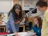 A teacher helping students in the classroom while looking through a textbook