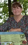 Smiling Wendi J. W. Williams  Caucasian female (she /ella) with brown hair leaning against trailside bilingual signage about riparian habitats.