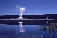 A geyser eruption is reflected in a lake at Yellowstone.