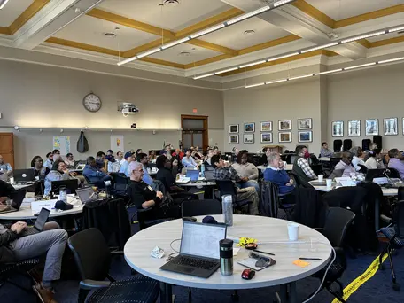 Room full of people sitting at tables listening to a speaker